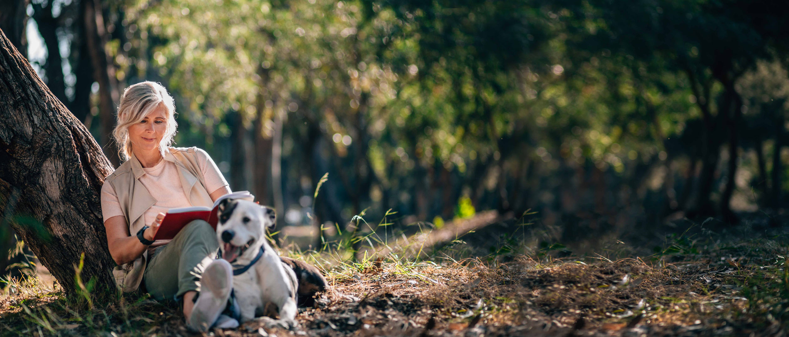 a woman sitting in the woods with a dog